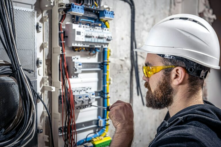 A male electrician works in a switchboard with an electrical connecting cable.